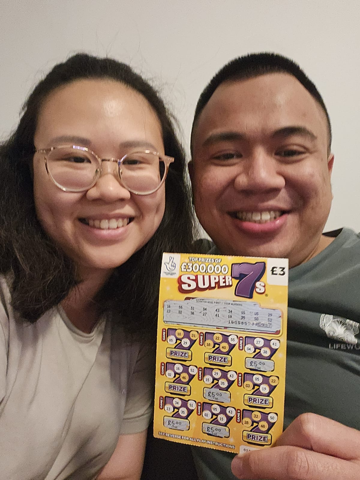 Angelia and Daniel smiling with a winning scratch card.
