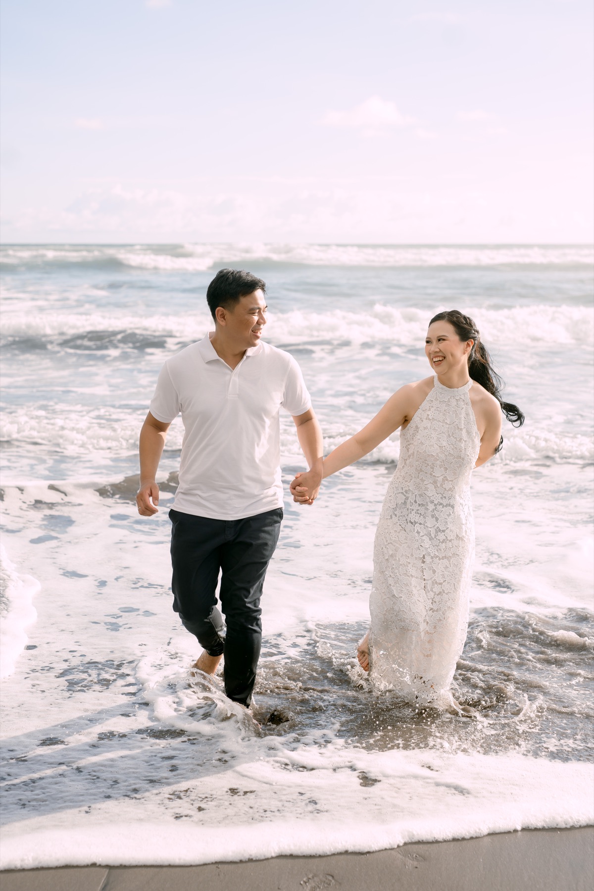 Angelia and Daniel walk hand in hand through the waves.