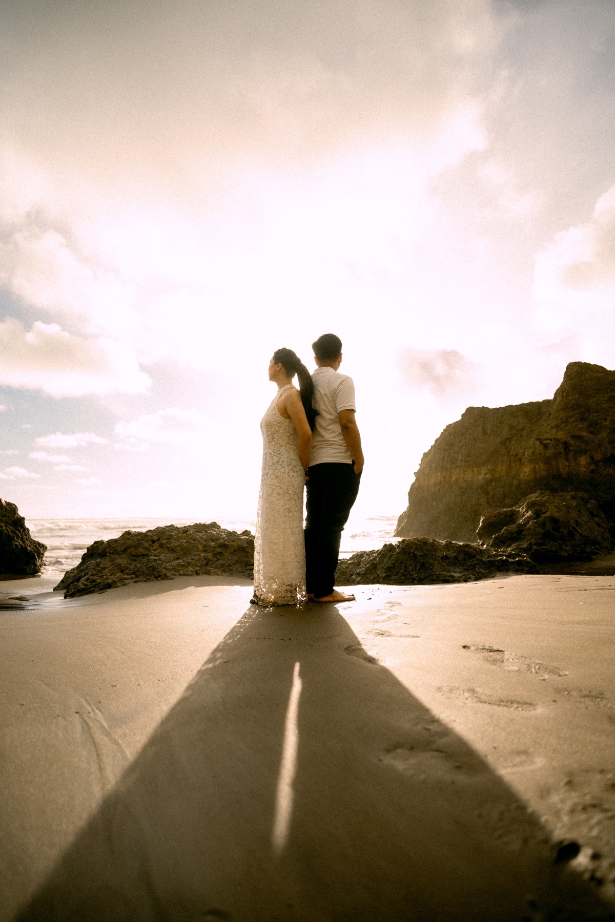 Angelia and Daniel stand back to back by the sea.